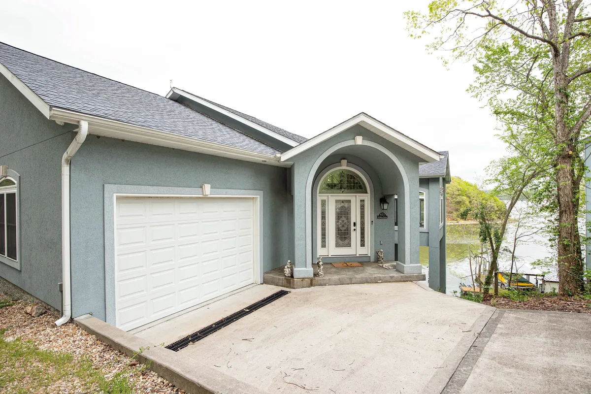 A broad exterior shot featuring the property’s front entrance, garage door, manicured landscaping, and a visible lake view in the background. The space is inviting, suitable for family gatherings, outdoor meals, and launching into lake adventures.
