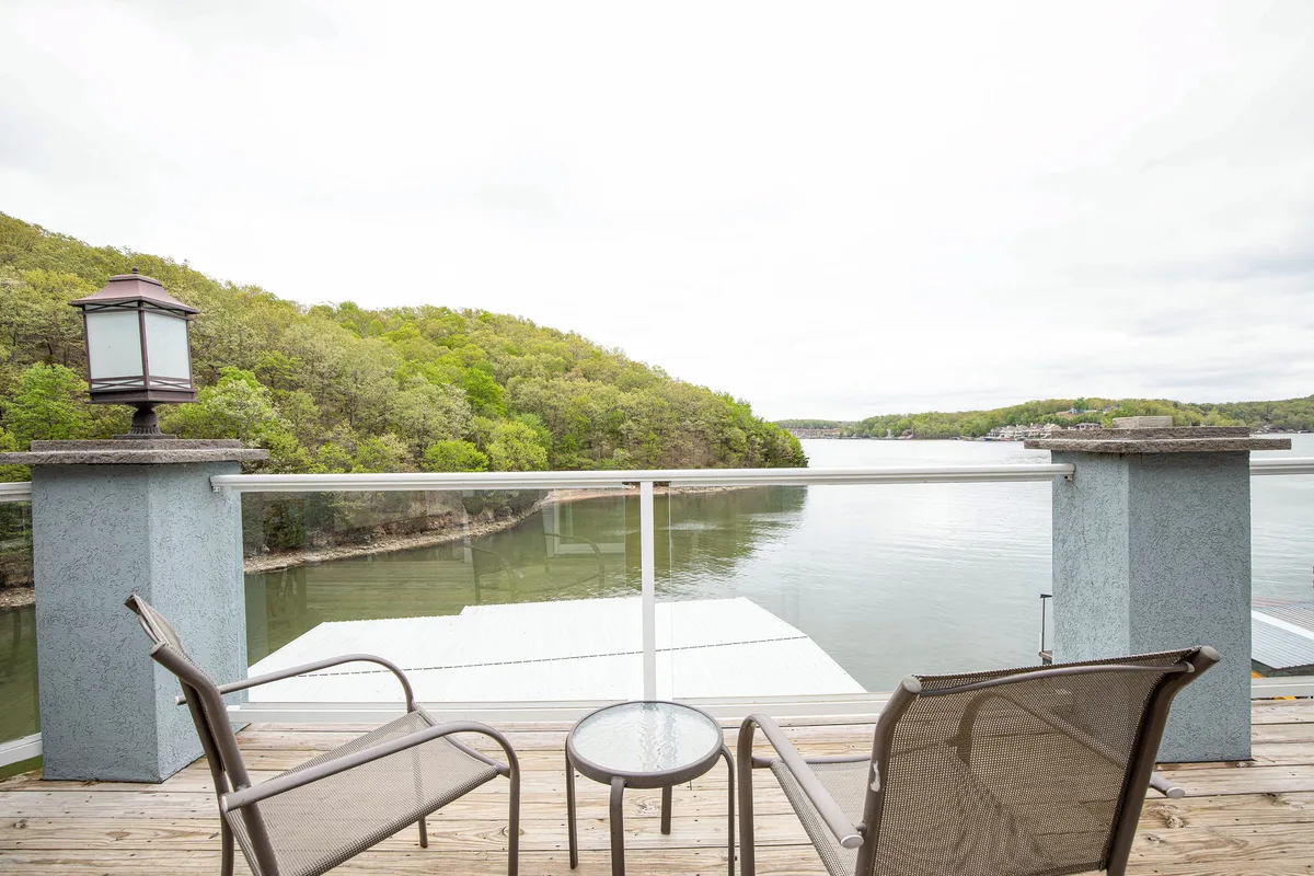A scenic view of the lake with calm waters, green rolling hills, and inviting outdoor seating. The area appears perfect for relaxing, reading, or sharing time with family and friends in a peaceful natural setting.