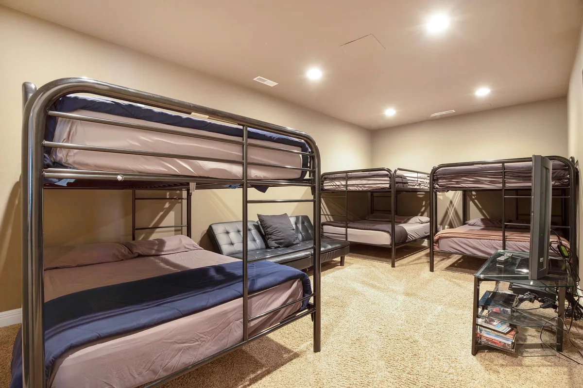 A cozy and inviting kids’ bunk room with multiple bunk beds, a sofa, and a television. The room is designed for group activities, sleepovers, and fun, offering ample space for children to play, watch movies, or relax together.