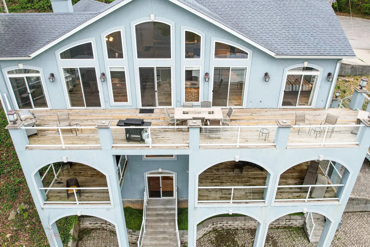 The image displays a spacious deck featuring an outdoor dining set and grill, framed by arched windows and offering scenic views. The setup is ideal for barbecues, group meals, and relaxed socializing in an open-air environment.