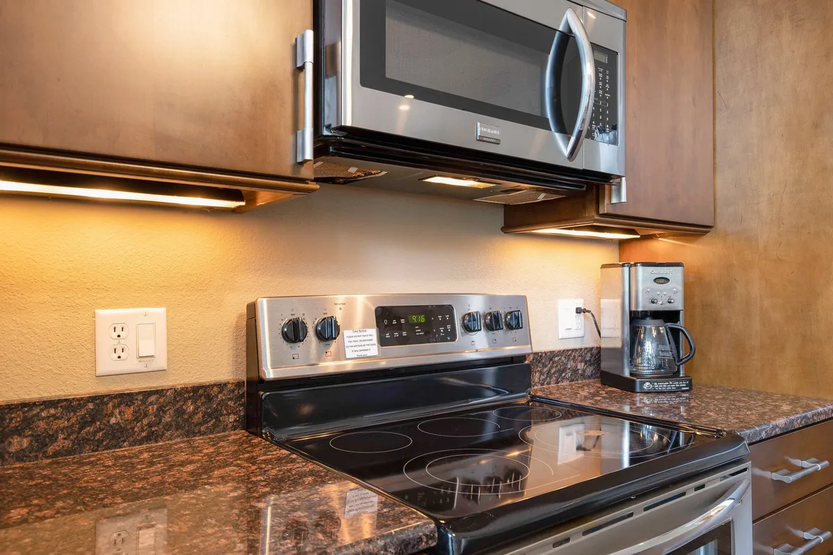 This image highlights a modern kitchen setup featuring a stainless steel microwave, glass top stove, coffee maker, and granite countertops. The space is brightly lit and organized, with everyday essentials easily accessible, evoking a sense of thoughtful provisioning and convenience.