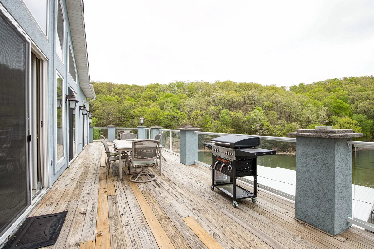 A spacious wooden deck overlooking the water, complete with a grill, dining table, and greenery all around. The setup conveys an inviting space for post-adventure lounging, group meals, and socializing with scenic lake views in the background.