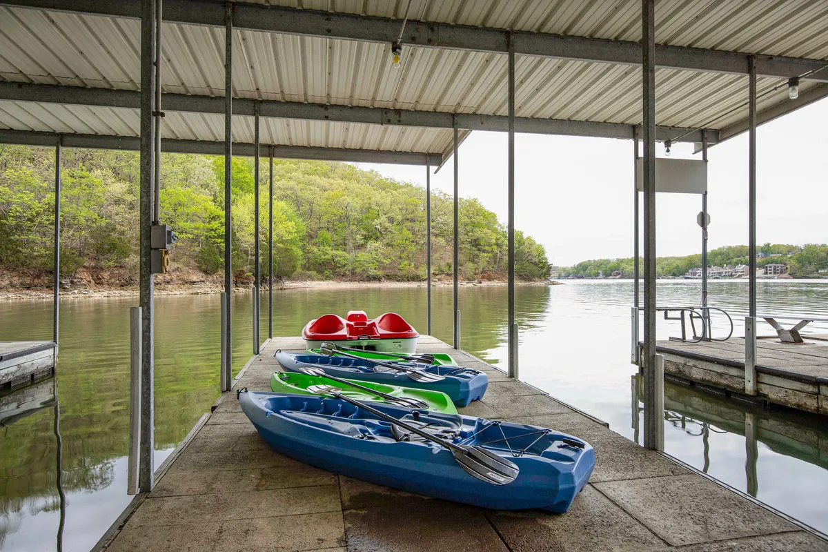 This image features a peaceful dock scene with kayaks resting on the dock, still water stretching out into the distance, and lush greenery framing the setting. The dock structure is sturdy and inviting, set up perfectly for water activities like kayaking, fishing, or simply relaxing close to nature.