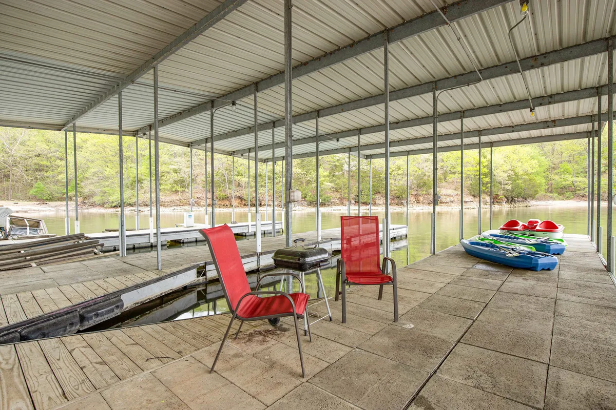 A close-up view of a lakeside dock featuring vibrant red chairs and kayaks ready for use. The scene emphasizes the recreational equipment available and the inviting atmosphere for relaxing or preparing for water activities.